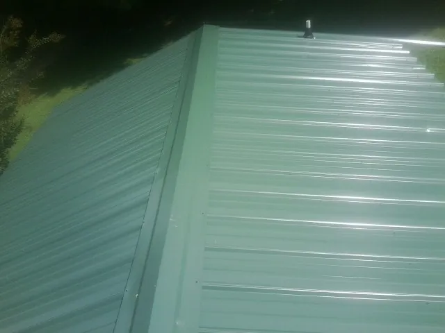 New green metal panels meeting at the ridge of a roof — Flat Roof Repair work by our crew in Rossville