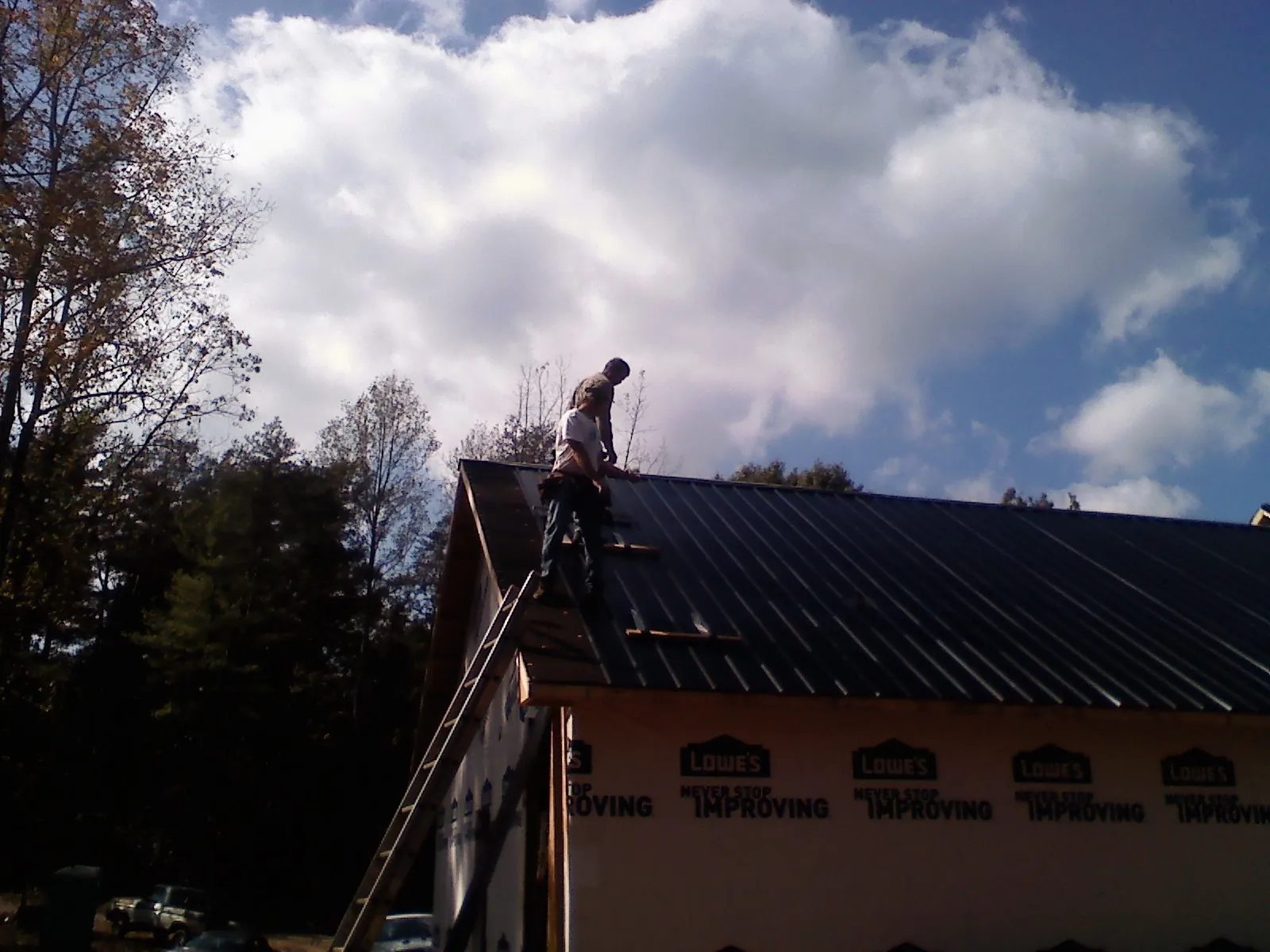 Roofer fastening dark metal panels high against a cloudy sky, from a Roof Inspection job in Rossville